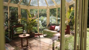 A conservatory with a wooden floor, a cushioned seating area, and potted plants. - Aquila Nova Retreat (The Patch)