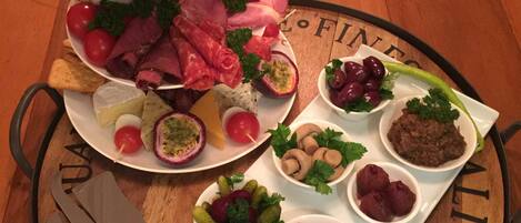A wooden serving tray with a variety of food items including fruits, cheeses, and meats, arranged on a table with a wooden surface.