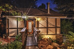 A rustic house with a wooden staircase leading to a door, surrounded by greenery and a stone pathway. - Aquila Nova Retreat (The Patch)
