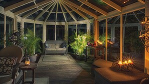 A covered patio with wicker furniture, potted plants, and ambient lighting. - Aquila Nova Retreat (The Patch)