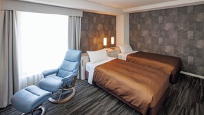 A hotel room with a bed, a seating area with a chair, a bedside table, and a wall-mounted light fixture. - J Hotel Rinku (Tokoname)