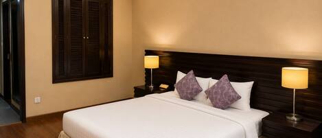A hotel room with a large bed, two bedside lamps, a wooden headboard, and a window with dark shutters.