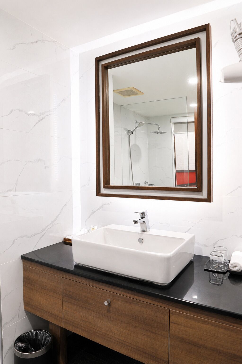 Un baño con lavamanos blanco, tocador de madera y un espejo con marco de madera.