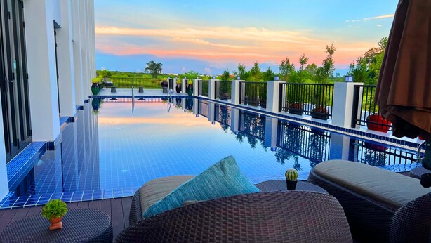A rooftop infinity pool with a view of the sunset, surrounded by outdoor seating and potted plants. - Savan Resorts (Savannakhet)