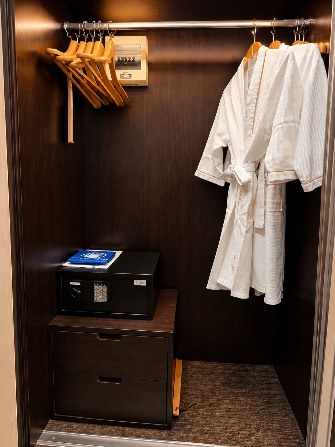 Une chambre d’hôtel avec une armoire en bois, un minibar et un peignoir accroché à la porte.