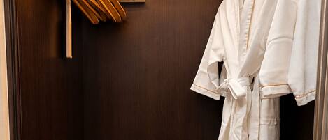 A hotel room with a wooden wardrobe, a minibar, and a robe hanging on the door.