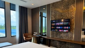 A hotel room with a bed, a desk, a chair, a TV mounted on the wall, and a view of the outdoors. - Savan Resorts (Savannakhet)
