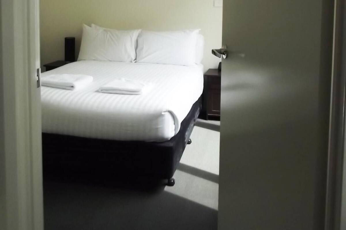 A hotel room with a bed, a nightstand, and a door.