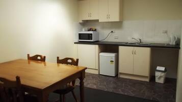 A small kitchen with a wooden table and chairs, a microwave, a mini fridge, and a sink.