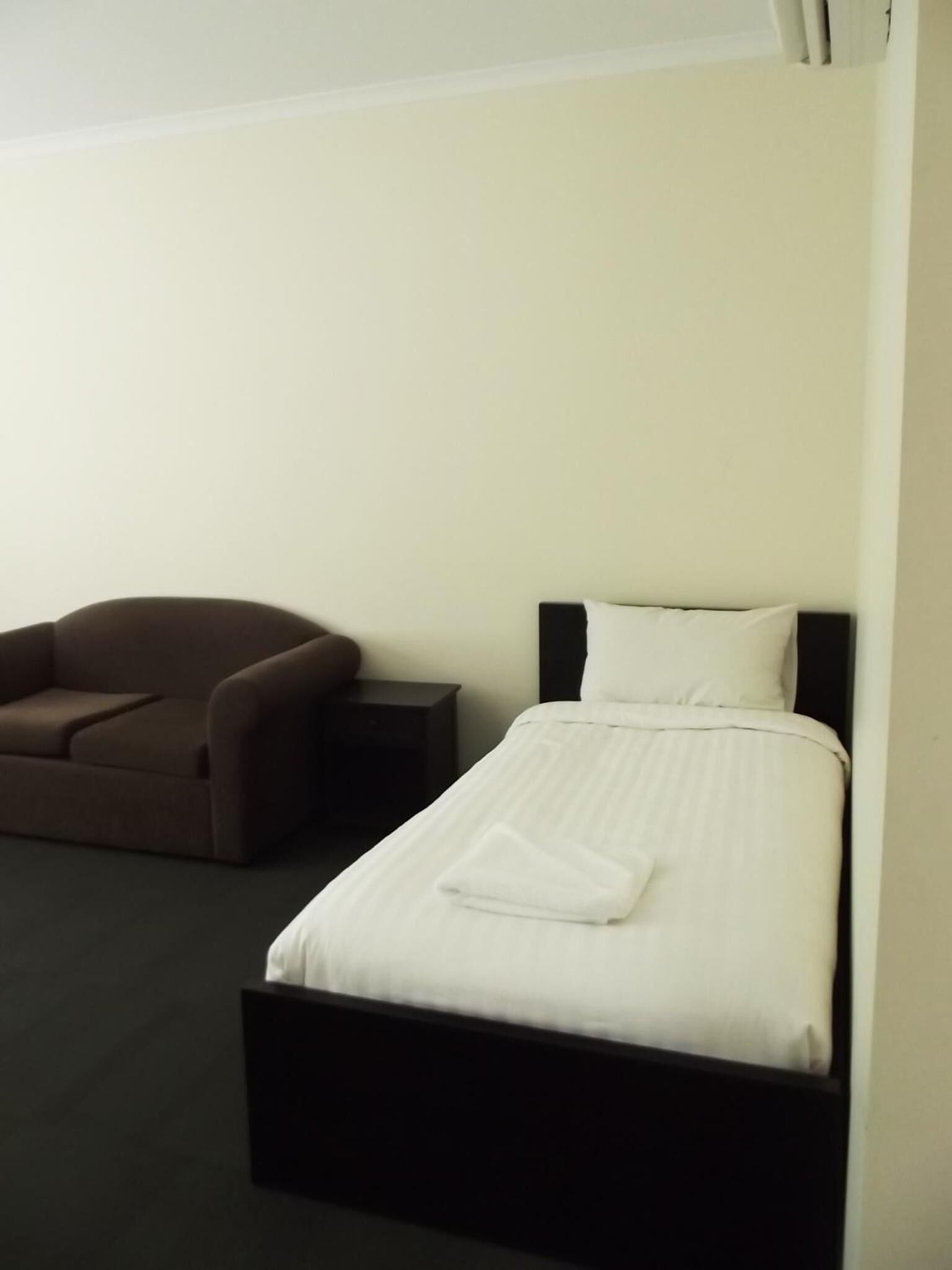 Una habitación de hotel con una cama individual, un sofá marrón y una mesita de noche pequeña.