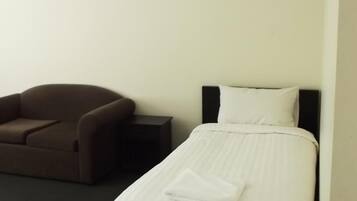 Una habitación de hotel con una cama individual, un sofá marrón y una mesita de noche pequeña.