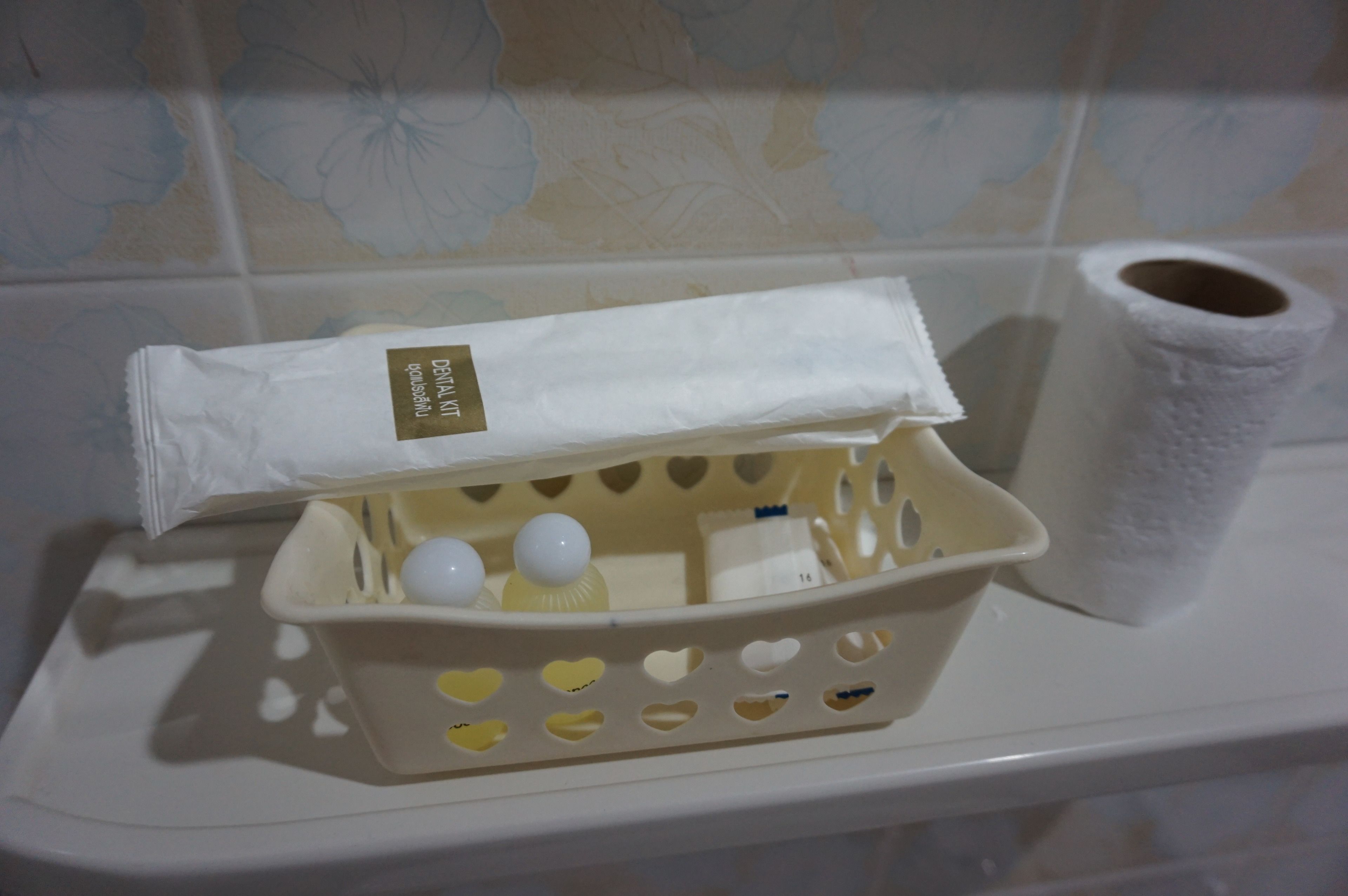 A bathroom with a white toilet, a tissue roll, and a basket with heart-shaped cutouts containing toiletries.