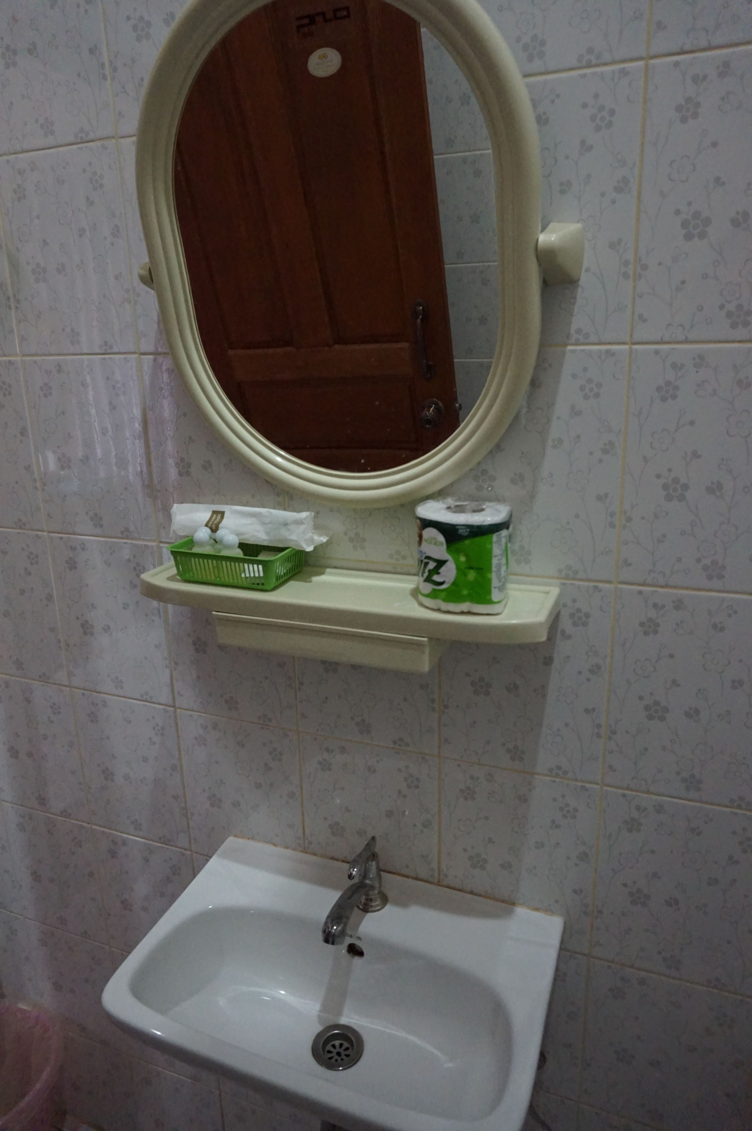 Un bagno con un lavandino bianco, uno specchio sopra e un cesto verde appeso al muro.