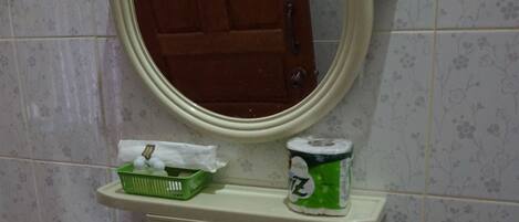 Un bagno con un lavandino bianco, uno specchio sopra e un cesto verde appeso al muro.