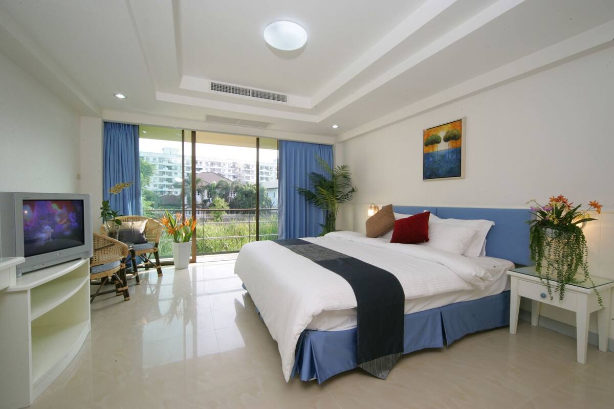 A modern hotel room with a large bed, a TV, a balcony with a view, and a painting on the wall.
