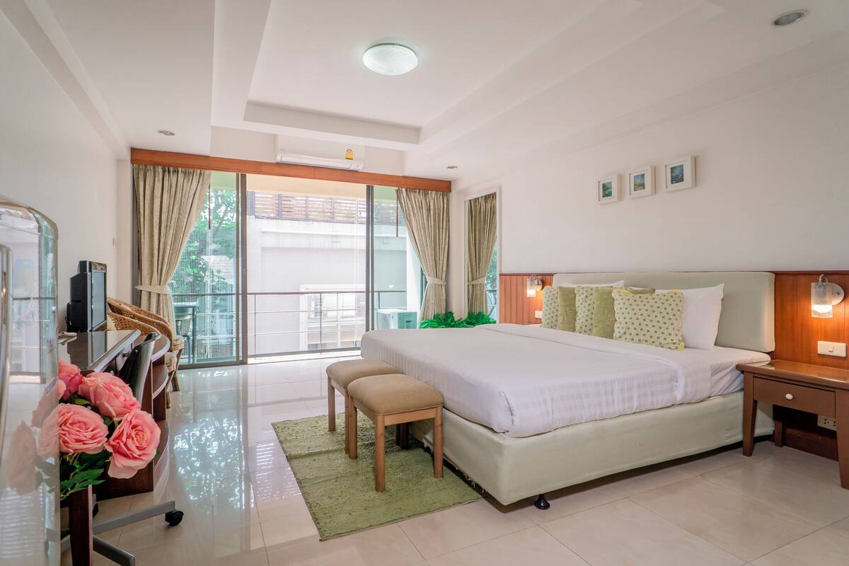 A modern hotel room with a large bed, a desk, and a balcony with curtains.