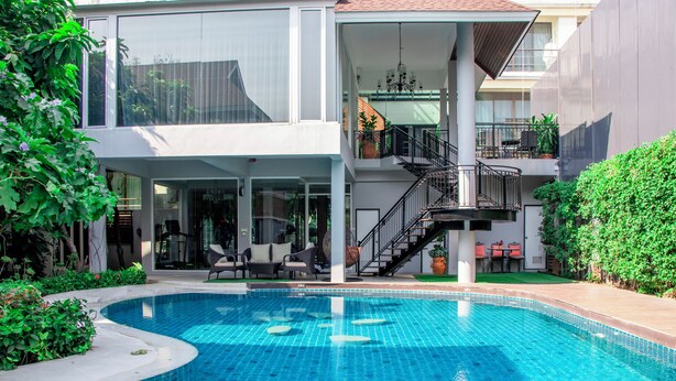 Ett modernt hus med en swimmingpool, utomhusmöbler och en trappa som leder upp till en balkong.