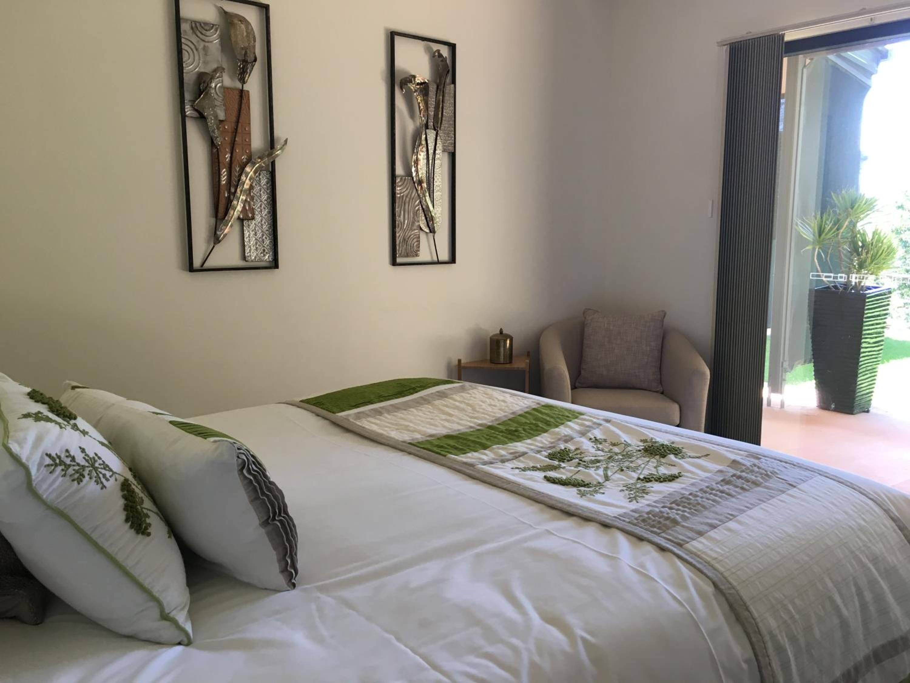 Une chambre avec un lit, deux œuvres d’art encadrées accrochées au mur, une chaise et une vue sur la verdure à l’extérieur.