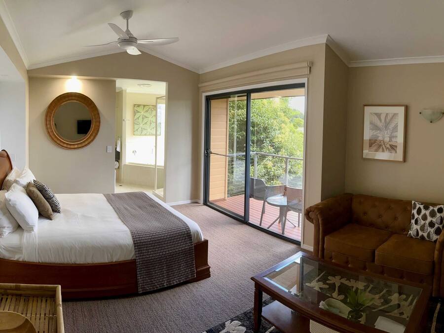 Une chambre d’hôtel comprenant un lit, une table basse en verre, un canapé, un ventilateur de plafond et un balcon aménagé avec du mobilier d’extérieur.