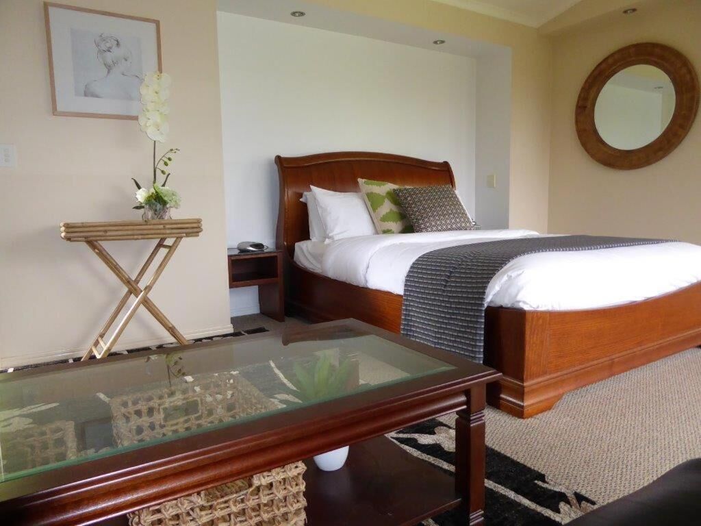 A bedroom with a wooden bed, a glass coffee table, a bedside table with a lamp, and a framed picture on the wall.