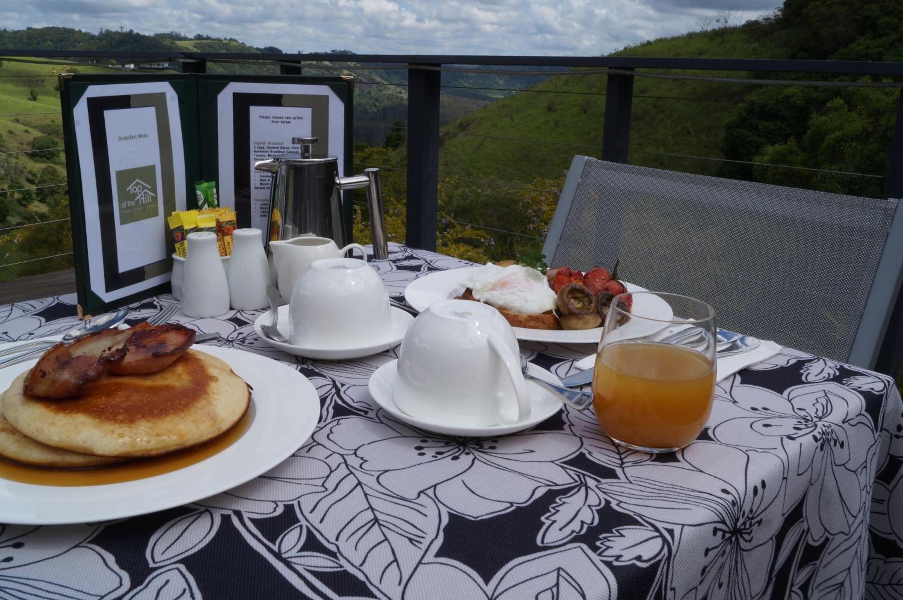 Taula de petit esmorzar amb crepes, ous i un got de suc, amb una vista panoràmica de fons.