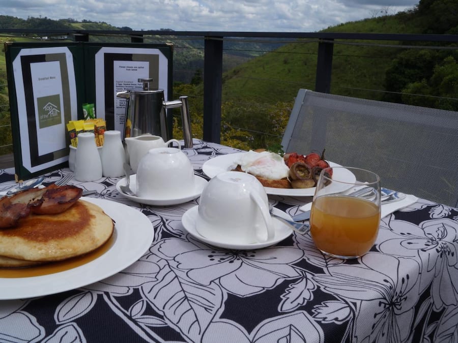 Una mesa de desayuno con panqueques, huevos y un vaso de jugo, frente a una vista panorámica.