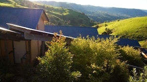 A building with a blue roof, surrounded by lush green hills and trees. - Top of The Hill (Bald Knob)
