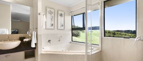 A modern bathroom with a large bathtub, a double sink, and a large window offering a view of the outdoors.