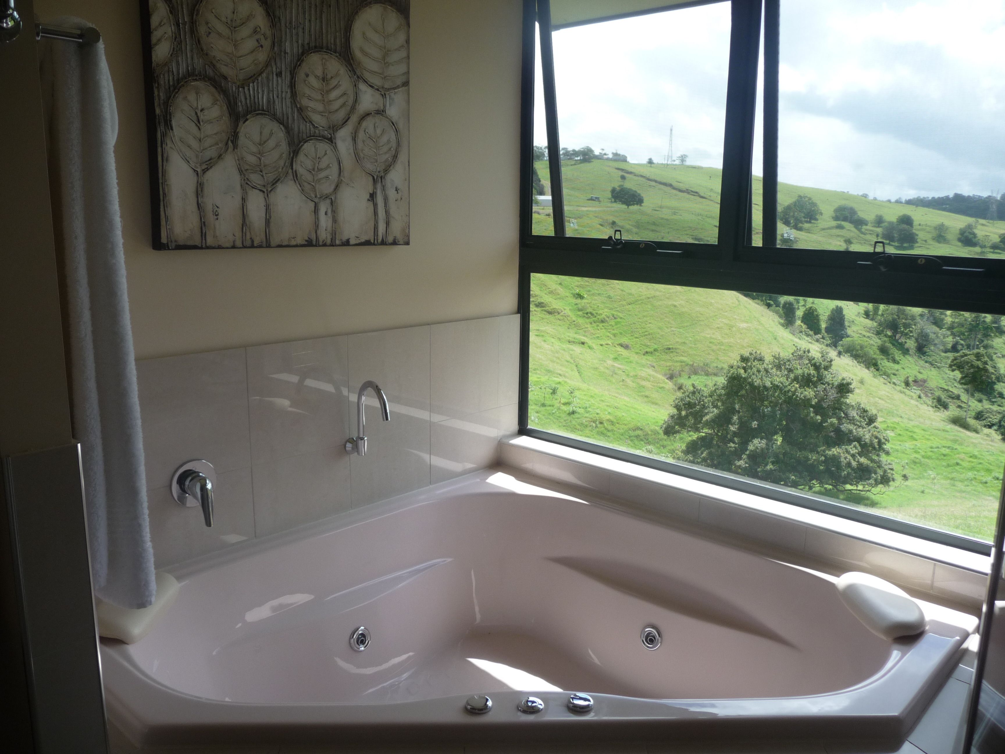 A bathroom with a large bathtub, a shower, and a window offering a view of a green landscape.