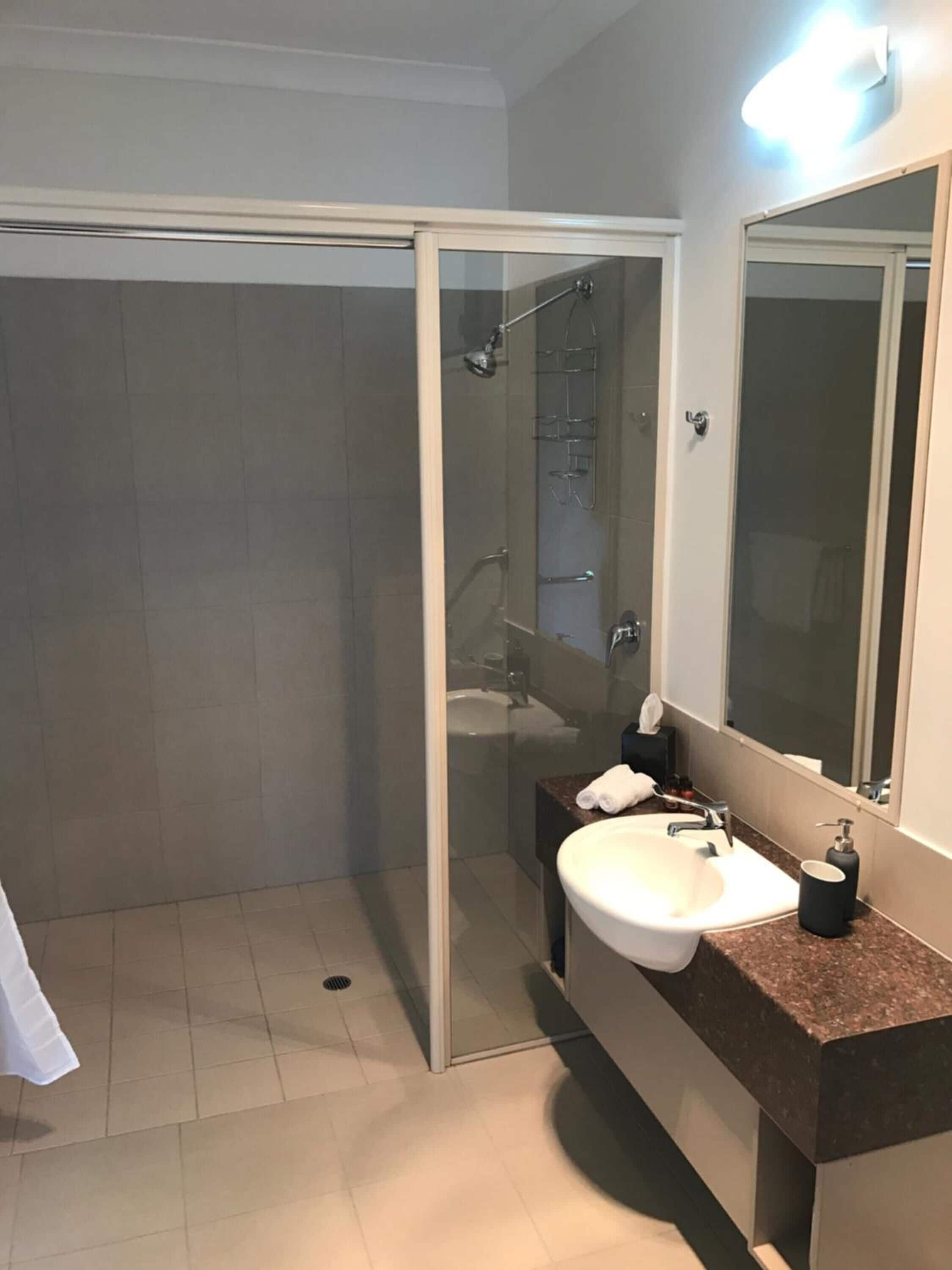 Une salle de bain moderne avec une douche à parois de verre, un lavabo doté d’un plan de travail en marbre et un grand miroir.