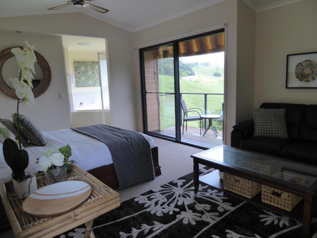 A bedroom with a bed, a coffee table, a sofa, a large window, and a balcony.