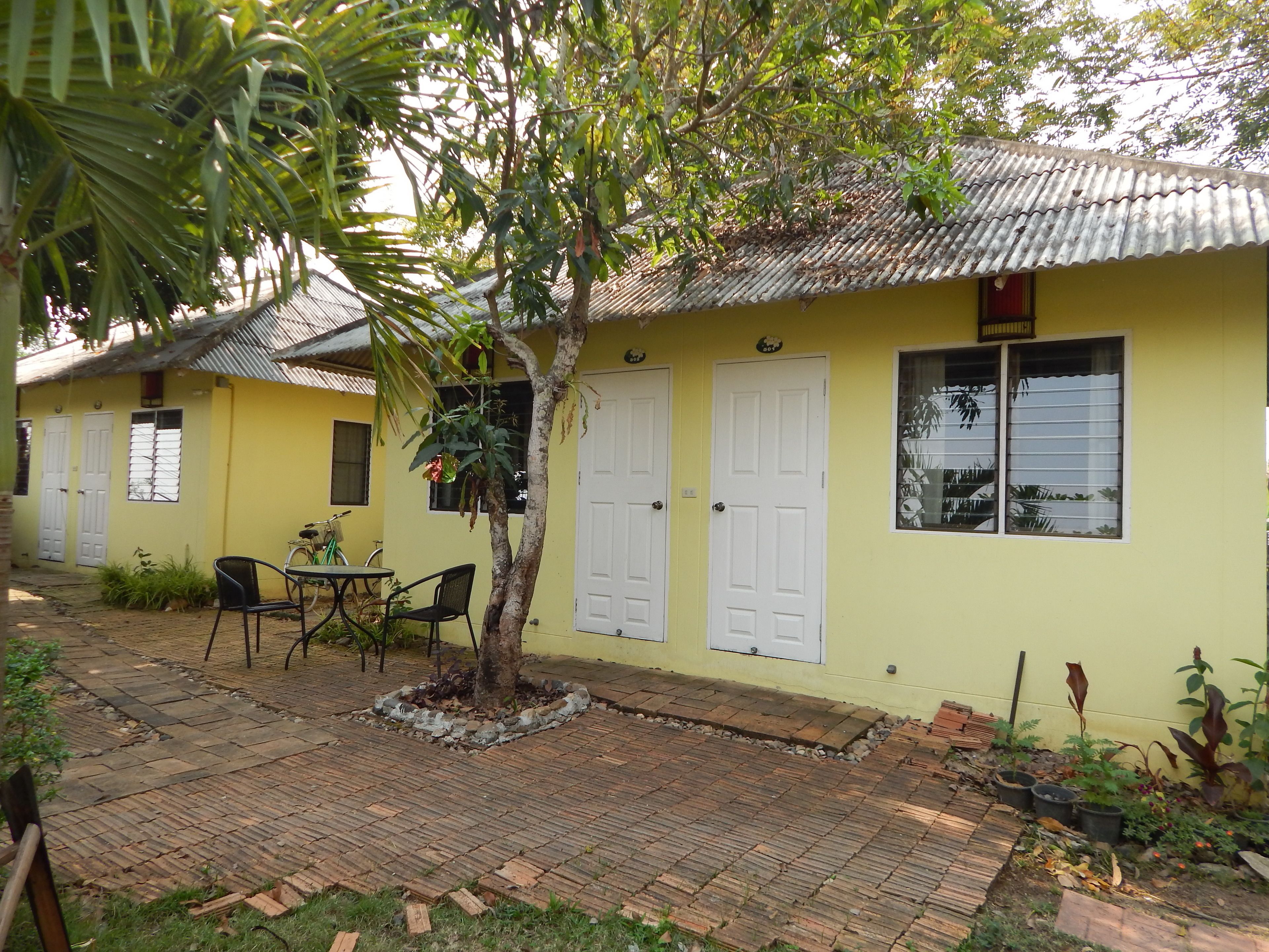 A yellow building with two white doors, a small table with chairs, and a tree in the center.