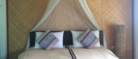 Uma cama com dossel, almofadas estampadas e um abajur ao lado.