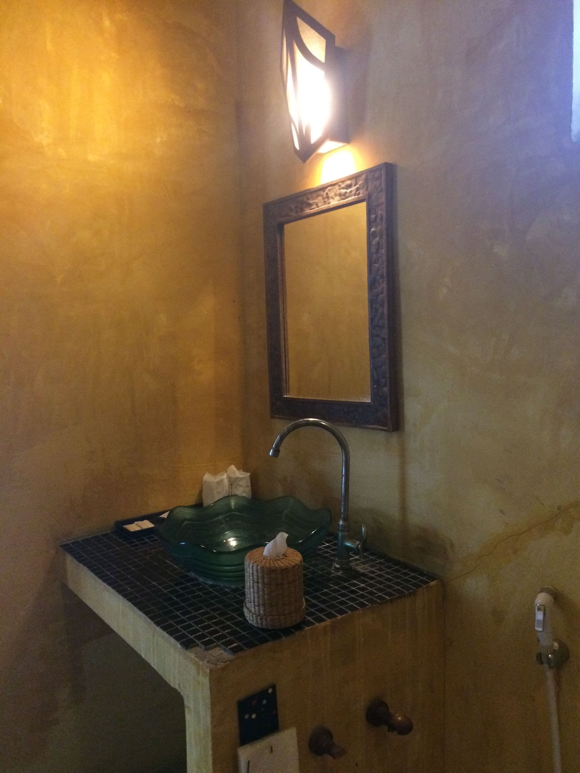A bathroom with a green sink, a mirror, and a towel dispenser.
