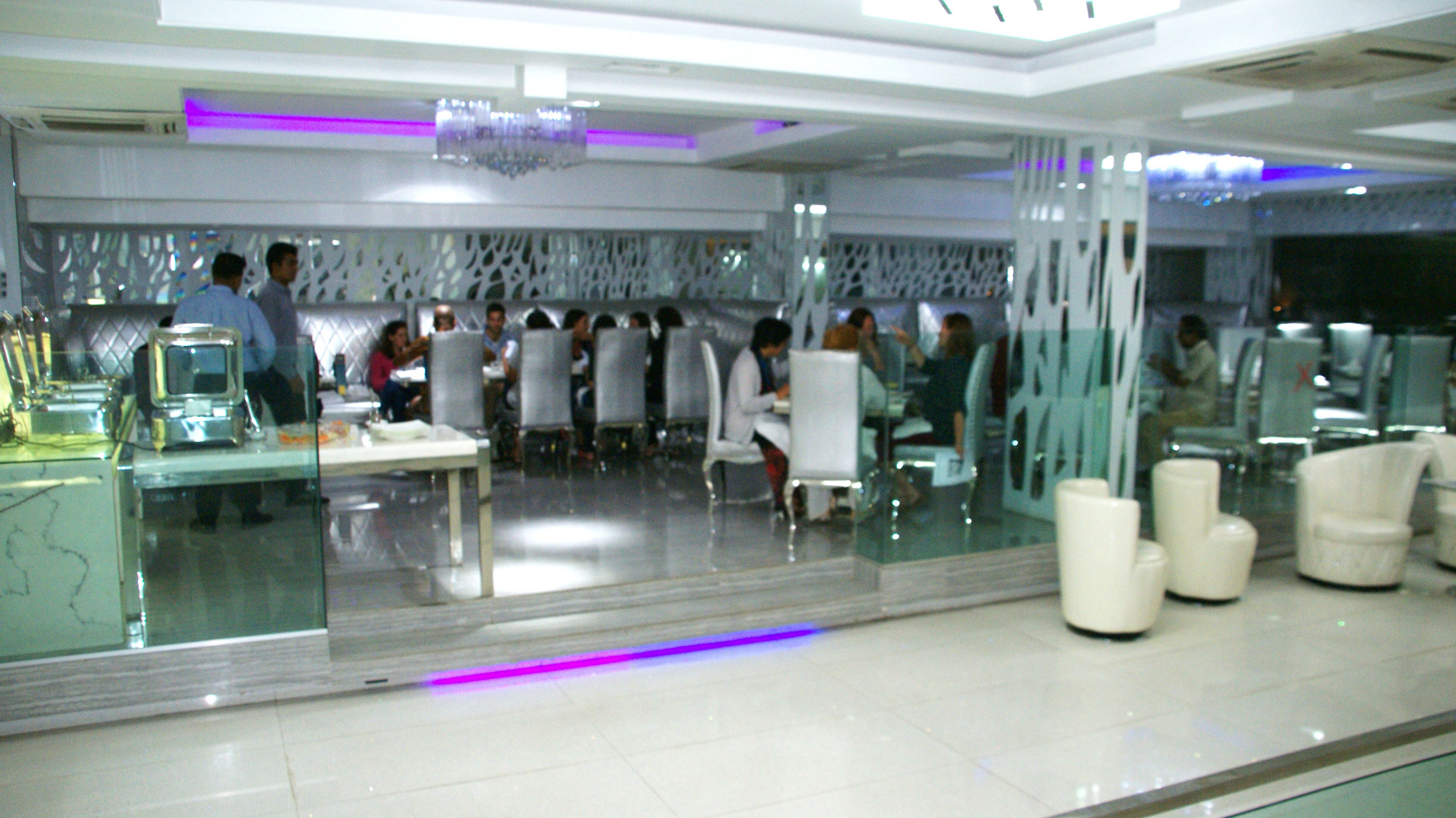 A modern restaurant with glass partitions, white furniture, and purple lighting accents.