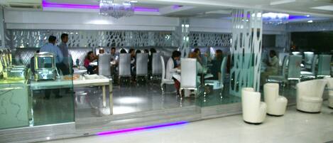 A modern restaurant with glass partitions, white furniture, and purple lighting accents.