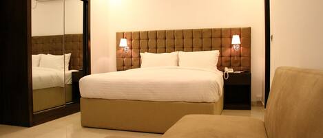 A hotel room with a large bed, two bedside lamps, a nightstand, a mirror, and a sofa.