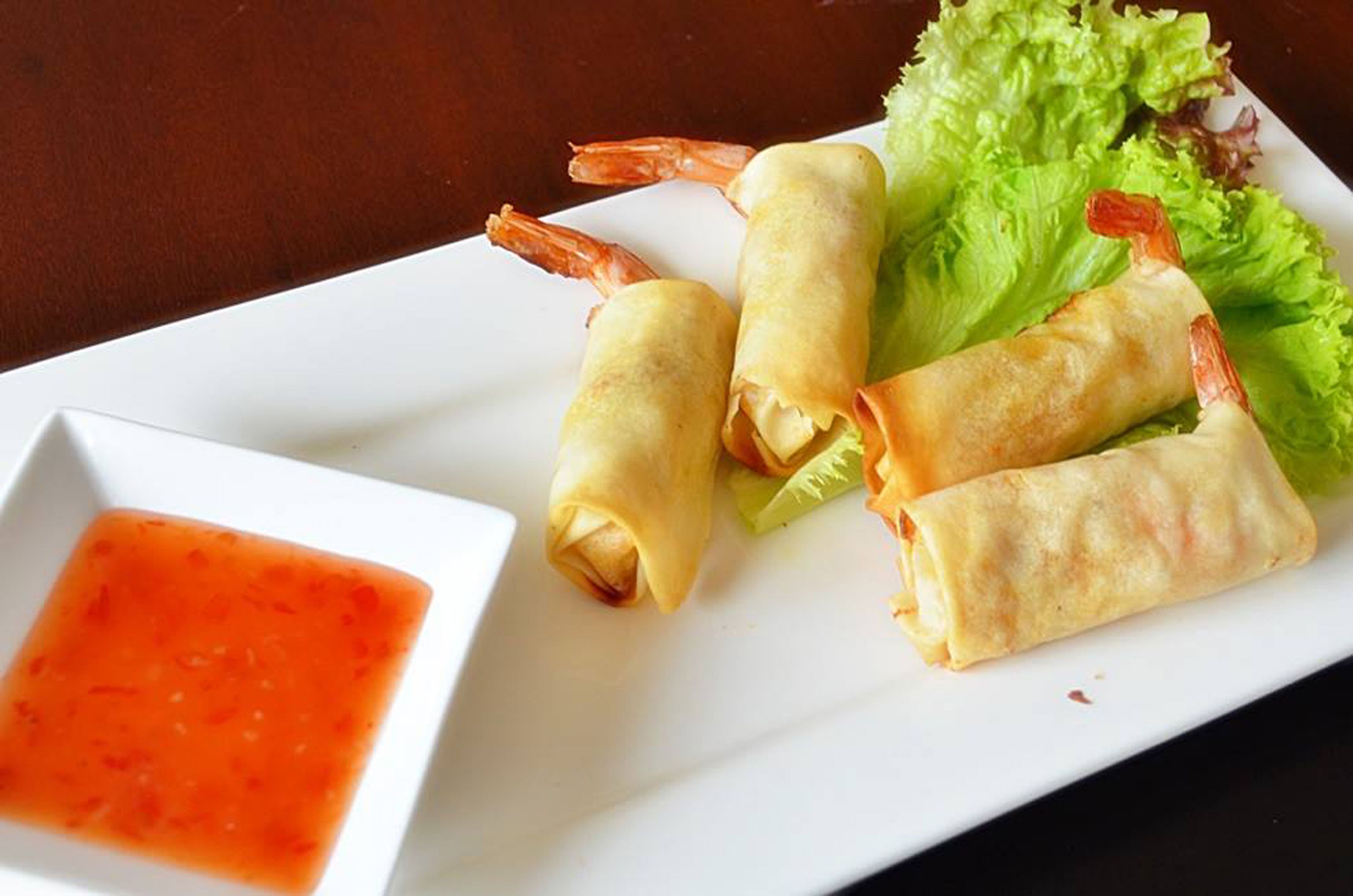 A plate with spring rolls, lettuce, and a small bowl of sauce.