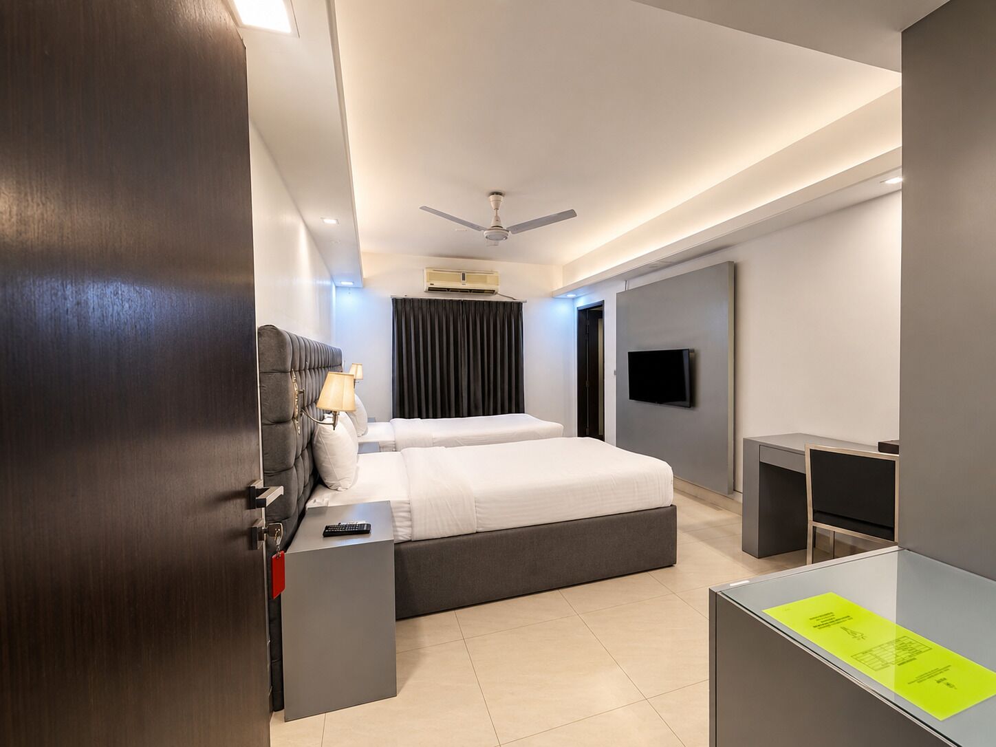 A modern hotel room with a bed, bedside tables, a TV, and a ceiling fan.