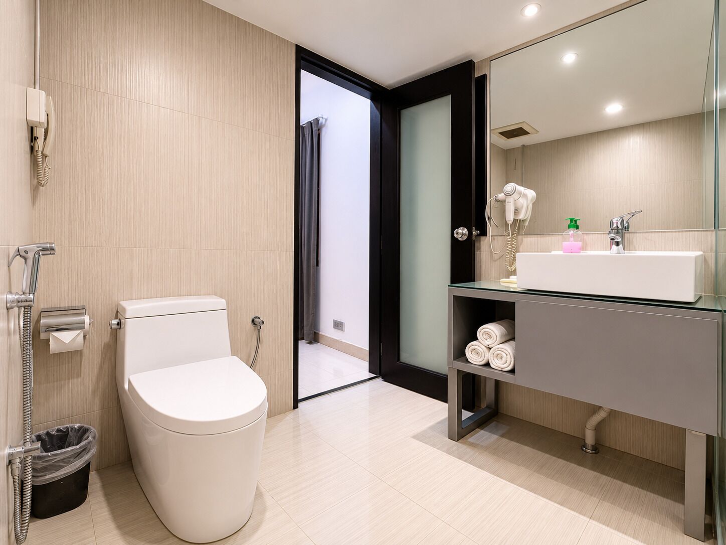 A modern bathroom with a toilet, a glass shower enclosure, a vanity with a sink, and a hairdryer.