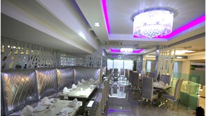 Een modern restaurant met een lange eettafel, comfortabele zitplaatsen en een kroonluchter.