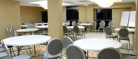 A conference room with multiple round tables and chairs, a whiteboard, and a patterned floor.
