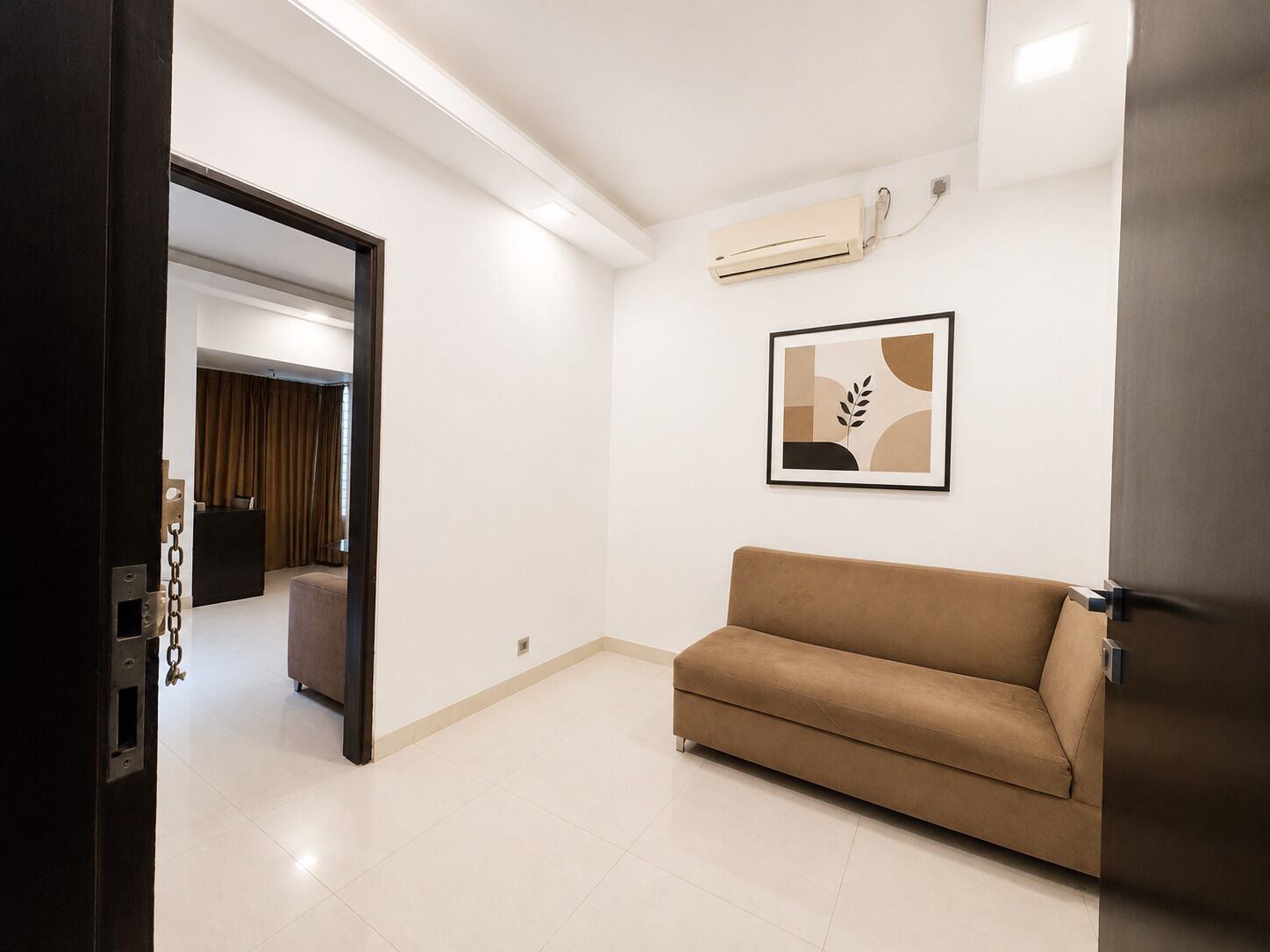 A modern room with a beige sofa, a wall-mounted air conditioner, and a framed abstract artwork.