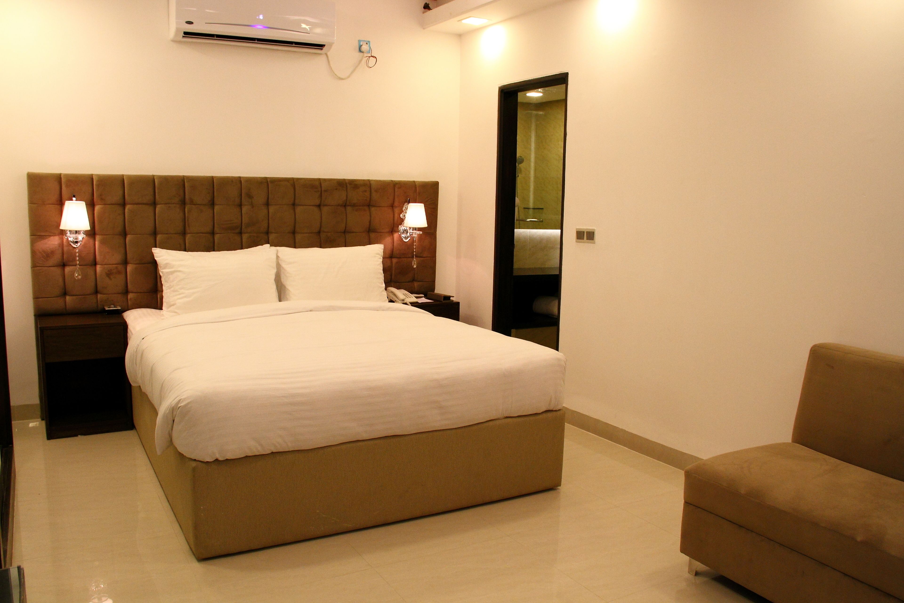 Habitación de hotel con una cama grande, dos lámparas de noche, una mesita de noche, un sofá y un espejo.