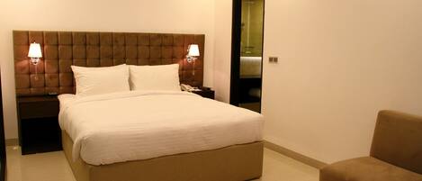 Habitación de hotel con una cama grande, dos lámparas de noche, una mesita de noche, un sofá y un espejo.