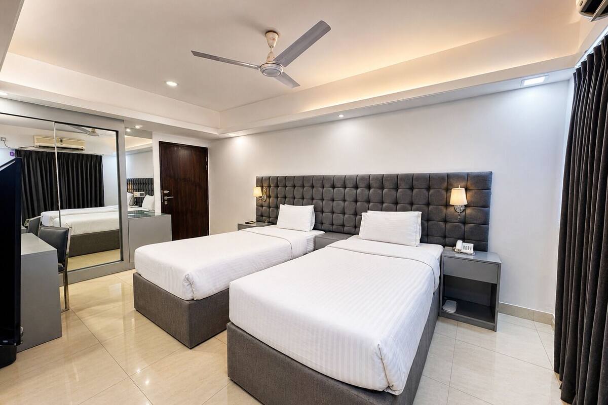 A hotel room with two beds, a ceiling fan, a desk, and a mirror.
