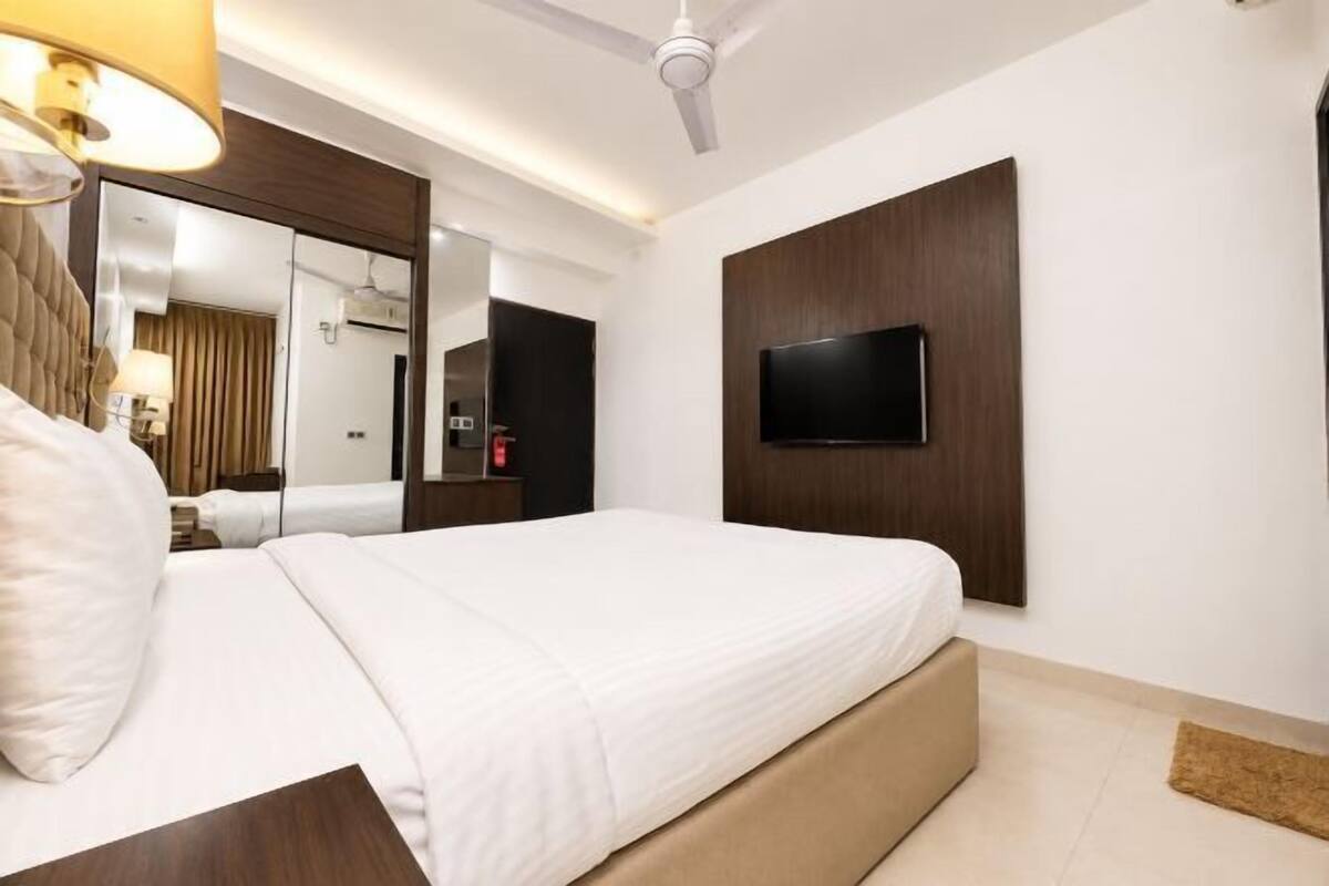 Una habitación de hotel con una cama, un televisor montado en la pared, un ventilador de techo y un espejo.