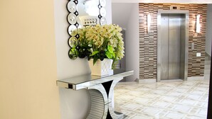 Een receptiegedeelte met een moderne console tafel, een vaas witte bloemen, een wandspiegel en een lift.