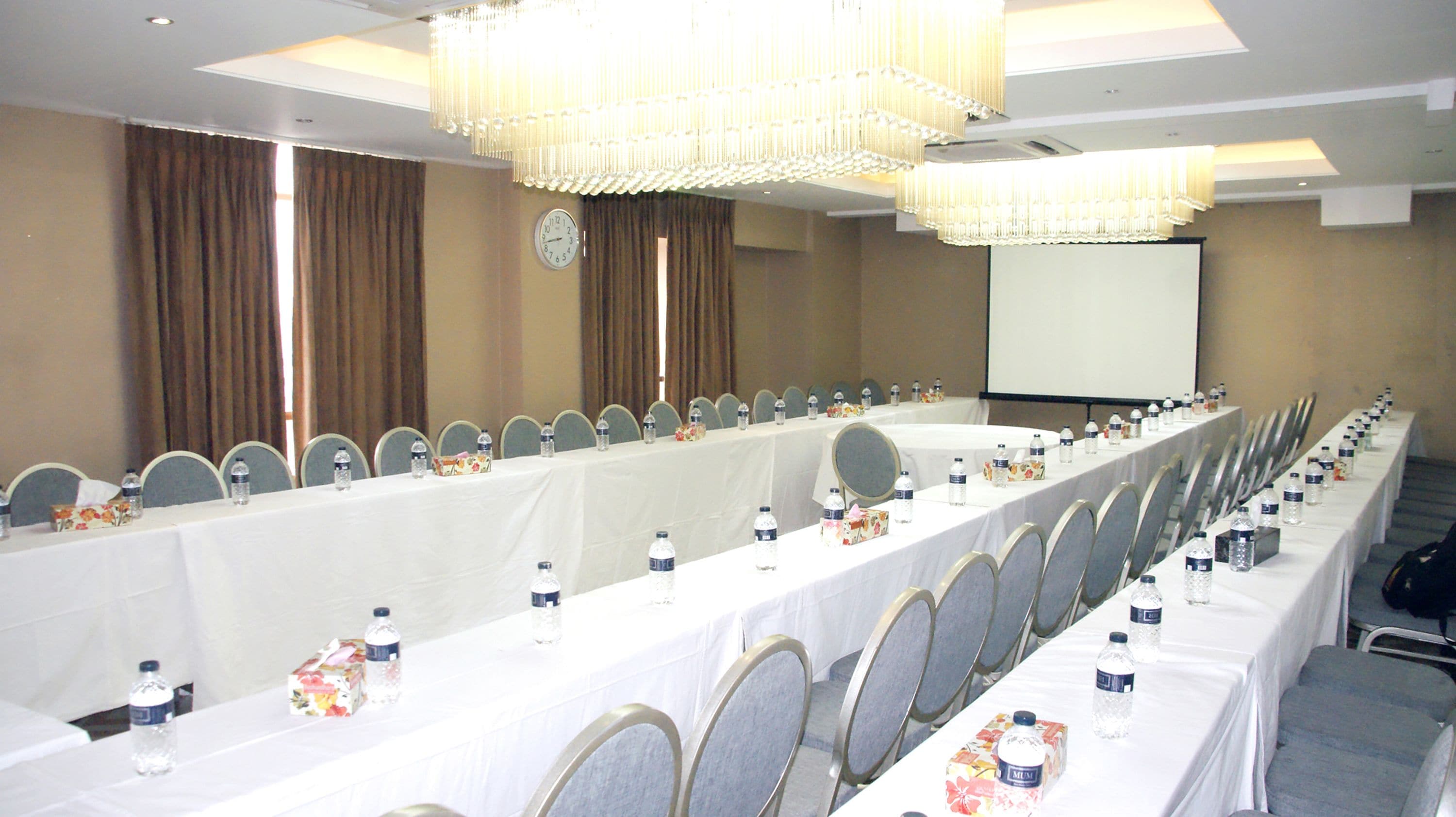 A conference room with a long table, chairs, water bottles, and a projector screen.