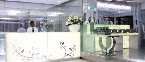 A reception area with a modern design, featuring a white reception desk with floral patterns, a glass display case, and a decorative vase with flowers.